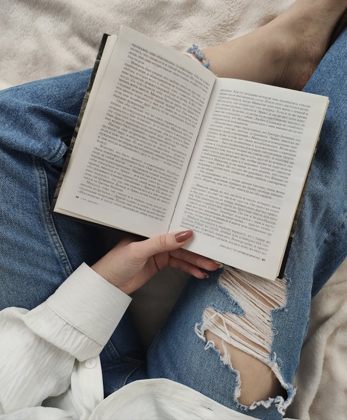 A woman enjoys a relaxing day reading a book while lounging indoors, dressed in casual jeans.